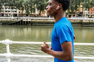 Energy in Motion: Young African American Man Running with Wireless Headphones by the River