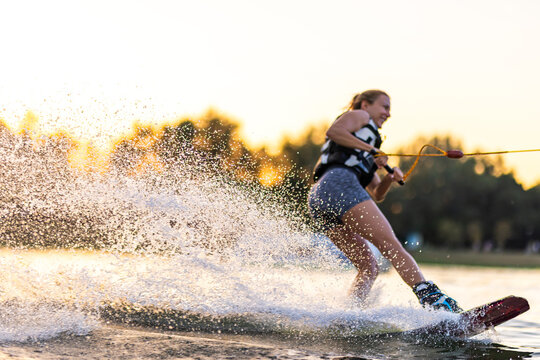 Female wakeboarder wakesurfing on sunset. Girl riding waterski cabel. Holding tow rope. Summer activities in the lake.