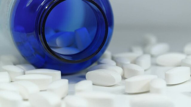 White pills scattered on table. Open blue container for nutritional supplements lies on table. Overdose. Biologically active sulfur pills in dosage 1500 mg. MSM for joints