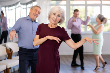 Elderly man and elderly woman dance energetic twist dance in studio..