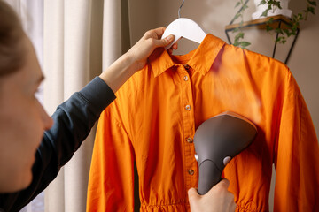 woman ironing dress with clothes steamer at home