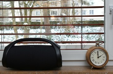 a sound column and a table round clock stand on the windowsill