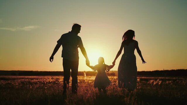 Daddy brings wife with daughter for run in evening field to pick fresh flowers to make bouquet for girls. Daddy and mother run happily with jumping daughter holding hands wishing evening to last
