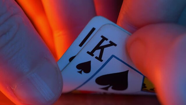 hand holds 10 and king, both spades, in a game of texas hold em poker with a dim, blue-toned background, suggesting a tense gambling scenario