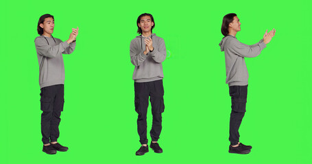 Asian happy guy applauding a person, clapping hands to show his congratulations and cheering for someone over full body greenscreen. Young man feeling optimistic and cheerful, standing ovation.