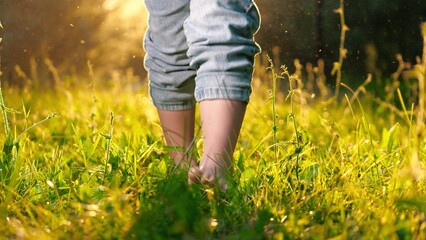 Small boy strolls barefoot through grass in field during summer vacation. Joyful boy walks shoeless...