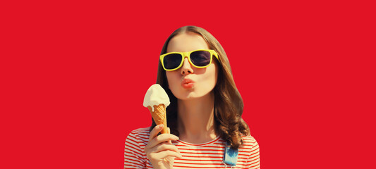 Summer portrait of happy young woman eating ice cream wearing sunglasses on red studio background