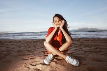 Carefree Fashionista Enjoying a Sunny Beach Vacation: Smiling Woman in Trendy Outfit, Sitting on Sand, Embracing the Wide Angle of Summer Lifestyle