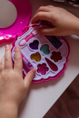 Cute little blonde girl does makeup with a set of baby cosmetics at home, little fashionista