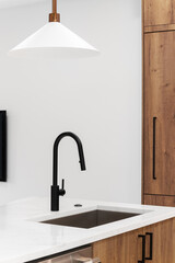 A kitchen faucet detail with wood cabinets, a black faucet, and gold light fixture hanging above...