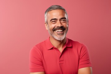 Portrait of a happy mature man in a red polo shirt on a pink background.