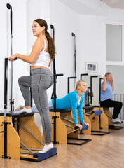Relaxed young woman wearing sportswear doing standing exercises on Pilates chair machine at gym indoors