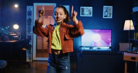 Happy young kid doing viral dance choreography, creating content to generate views and engagement. Cute girl having fun dancing around living room, entertaining audiences