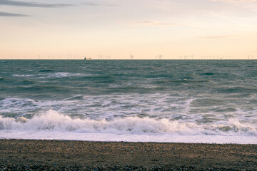 Shingle beach on a cloudy winter late afternoon, wind turbines offshore and a ship