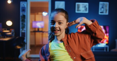Dutch angle shot of cute girl in neon lit apartment filming dance tutorial for other children...