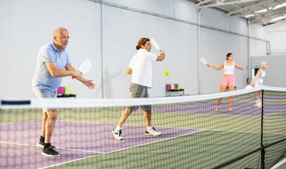 Two athletic men of different ages are playing a game of pickleball on a court inside a sports...