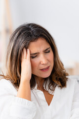 Vertical close-up of a woman gesturing headache and discomfort at home