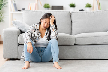 Desperate asian woman sitting at home hand in head with thoughtful expression