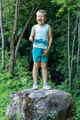 Naklejka premium A small boy climbs on a big stone in the forest and shouts loudly