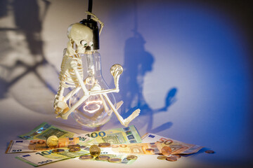Scared of high electricity prices, a toy human skeleton hangs on a lamp and looks at big money for...