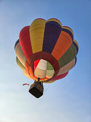 Looking up from directly below at a colorful hot air balloon as it is flying overhead with a plain blue sky as a background. © Janice