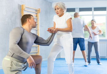Senior woman train in pair with middle-aged coach to strike and reflect blows of enemy. Intense...