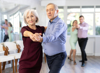Couple of elderly man and elderly woman dancing tango in studio