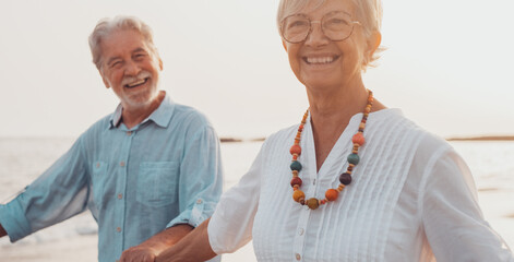 Couple of old mature people walking on the sand together and having fun on the sand of the beach enjoying and living the moment. Two cute seniors in love having fun. Barefoot walking on the water.