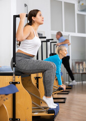 Concentrated young female making tone exercises for legs on Pilates chair equipment in gym. Active and healthy lifestyle concept