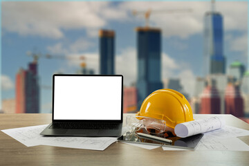 Yellow hardhat and laptop at a construction site, emphasizing safety and technology in the building...