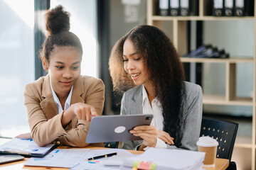 Two African businesswoman discuss investment project working and planning strategy with tablet laptop computer in office.