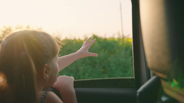 child girl face looks smiling from car out window, cook wind freedom travel, free girl catching wind from car window, schoolgirl, happy child travels, summer day, trip, cinematic, light moved by hand