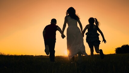 silhouette mother runs into sunset holding her son daughter hand, happy family running, boy girl,...
