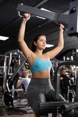 Fototapeta premium Portrait of concentrated sporty girl performing lever pull down on gym machine for strengthening back muscles. Sports and fitness concept