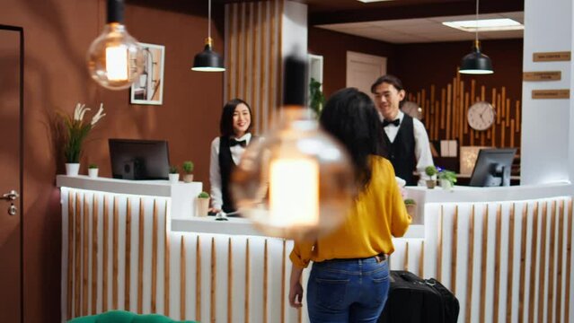 Hotel guest arriving early at reception after long flight, trying to do check in process with front desk staff. Receptionist greeting client with luggage, smiling and offering concierge services.