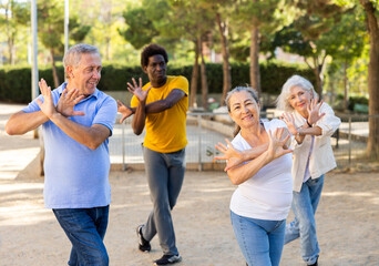 Group of cheerful mixed-race and various aged adult people doing aerobics and working out at park...