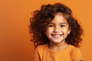 Portrait of a happy little girl with curly hair over orange background