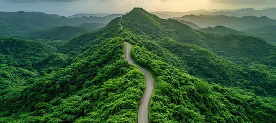 Aerial view of serpentine road cutting through lush forest towards majestic mountain summit.