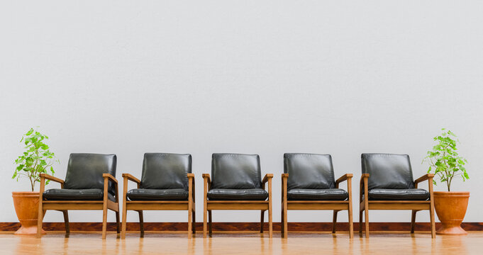 Row of five wooden chairs with black cushions near pots on white wall and cafe floor stage