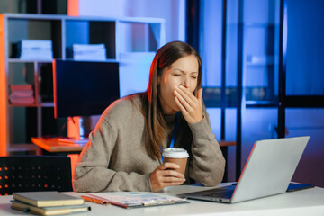 Business woman drinking coffee to get some energy for working overtime sitting at desk using computer and doing overtime