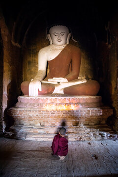 Novice monk praying in front of giant Buddha, Bagan, Myanmar