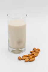 Glass of almond milk surrounded by almonds on a white background