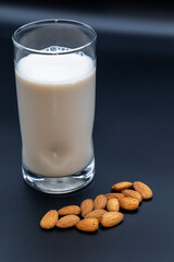 Glass of almond milk surrounded by almonds on a balck background