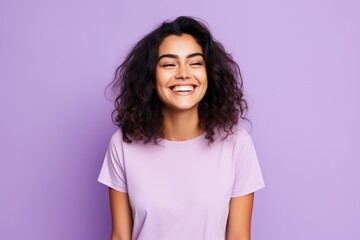 Portrait of a beautiful young woman laughing and looking at camera over purple background