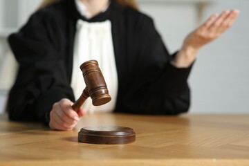 Judge striking mallet at wooden table in courtroom, closeup