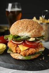 Delicious burger with crispy chicken patty and sauces on grey table, closeup