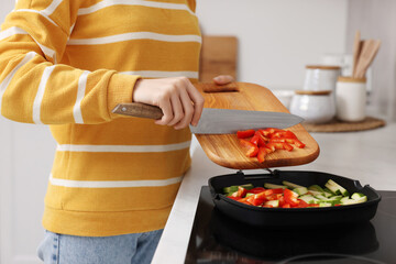 Cooking process. Woman adding cut bell pepper into pan with vegetables in kitchen, closeup