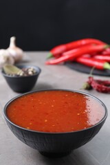 Spicy chili sauce in bowl on grey table