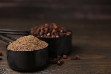 Aromatic clove powder and dried buds in scoops on wooden table, closeup. Space for text