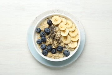 Tasty oatmeal with banana, blueberries and chia seeds served in bowl on white wooden table, top view
